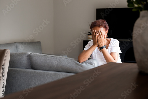 Sad senior hispanic woman covering her face with hands in living room