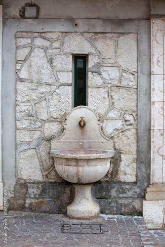 Old stone drinking fountain with a brass spout against a textured wall, Salo, Lake Garda, Italy