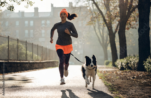 border collie running next to owner during morning jog, leash attached, city park trail, energetic dog, realistic sports lifestyle photo