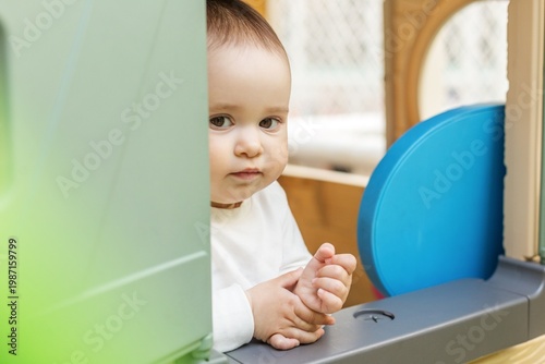 Cute toddler peeking from playhouse window and looking at camera