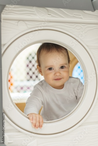 Cute toddler looking through round window of playhouse