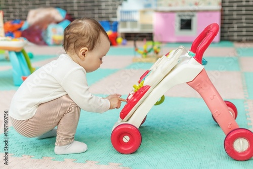 Toddler exploring activity walker toy while squatting on floor. Motor skills development.