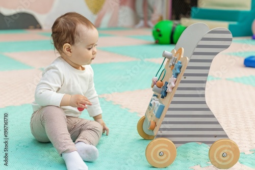 Toddler playing with educational activity walker toy on floor. Motor skills development.