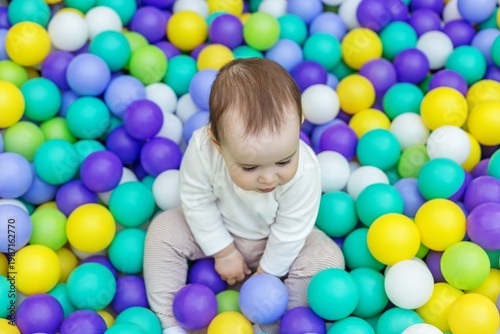 Toddler sitting in colorful ball pit in indoor playground. Top view