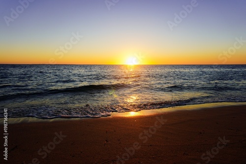 Фотография Warm sunset over a calm ocean shoreline with gentle waves and glowing reflections