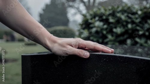 A gentle hand resting on a black gravestone in a peaceful cemetery capturing a moment of reflection and remembrance