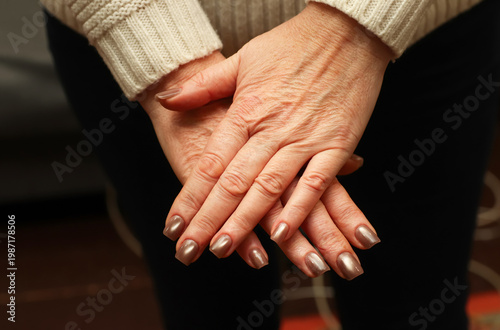 Close-up of a woman hands with professional bronze metallic manicure. Mature female hands crossed over dark clothing. Beauty and nail care concept