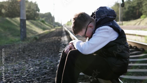 A boy sits on the train tracks after school, depressed because he is being bullied at school.