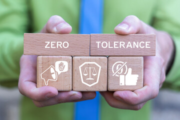 Concept of zero tolerance. Business person holding wooden blocks with icons sees the inscription ZERO TOLERANCE. Severely punishing all unacceptable behaviour.