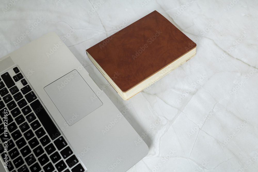 Fototapeta premium Minimal workspace with laptop and notebook on marble desk, representing modern office environment and organization.