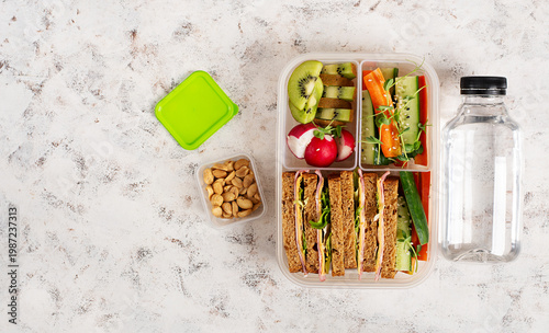 Healthy lunchbox with sandwiches vegetables fruits and water bottle top view
