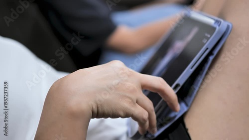 Close-up of a woman scrolling social media on a tablet while sitting near a child. The image reflects digital lifestyle, screen time behavior, and modern parenting environment.