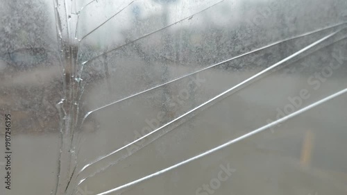 Close-up view of cracked glass showing progressive damage with visible lines and reflections, capturing the intricate details of the shattered surface in an outdoor setting