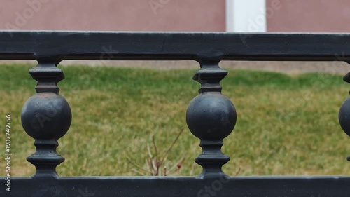 Black wrought iron fence with decorative balusters and spherical elements, showcasing a continuous view of the structure against a green lawn and pink wall background