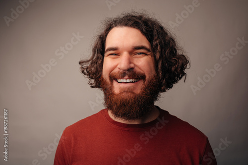 Smiling Bearded Man In Studio Celebrating Content Milestone, Relaxed Posture, Warm Lighting, Curly Hair