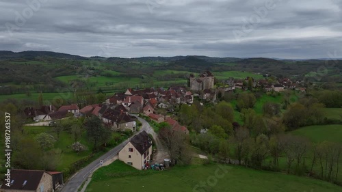 Aerial view of Curemonte France with Saint Hilaire castle overlooking the historic village nestled in lush green rolling hills under cloudy sky