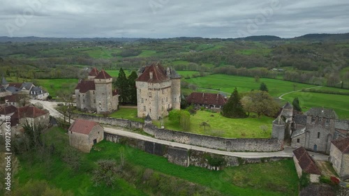 Aerial view of Curemonte France with Saint Hilaire castle and historic stone buildings overlooking lush green countryside under cloudy sky