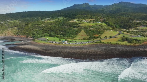 Surfers ride waves along the scenic coastline of Raglan, Waikato, New Zealand. The popular surf spot attracts visitors seeking adventure on the water.