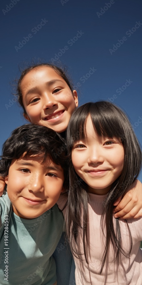 Obraz premium Three children smiling and embracing under clear sky