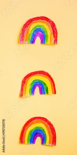 Triple hand drawn rainbows aligned on soft yellow paper backdrop