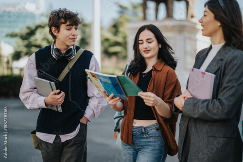 Three young students walk together while one reads from a notebook on a campus path. Friends chat and study casually outdoors near university buildings.