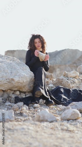 Woman in black dress sitting on rocks in desolate landscape