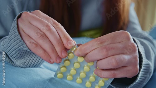 A young ill woman rests at home, placing medication in her mouth and drinking water from a glass. 