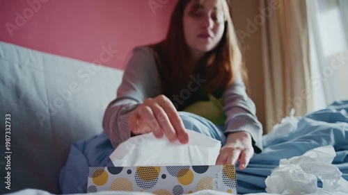 Close-up hand of uwell girl with a cold blowing her nose with tissues while resting in bed at home