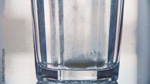 White soluble tablet dissolving in a glass of water, creating fizzy bubbles for health treatment. Macro shot