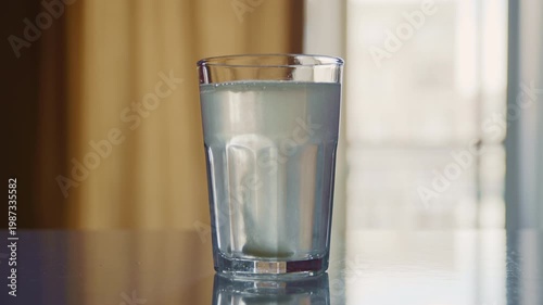 A healing tablet placed in clear water rapidly dissolves, producing carbonation and small particles swirling inside the glass. 