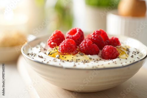 Close-up of Greek yogurt bowl with raspberries, chia seeds and golden honey drizzle, soft bokeh background in sun-drenched breakfast nook