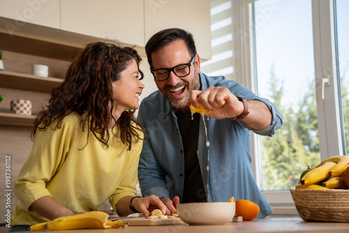 Fotografie Happy couple cooking fruit salad at home, husband squeezing lemon juice