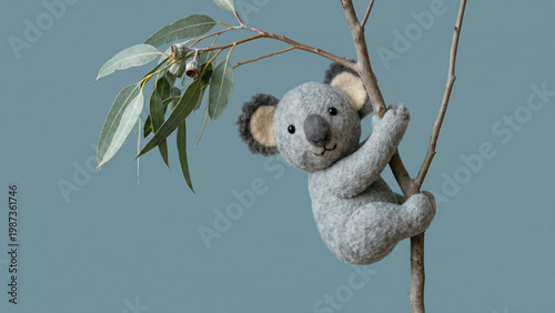 A handcrafted felt koala sculpture clings to a branch with eucalyptus leaves against a solid blue background with copy space.