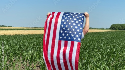 Foto Person holding a large United States flag in a green crop field under clear blue