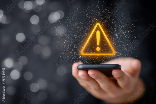 Close up of hand holding smartphone with glowing yellow triangle warning exclamation icon, cyber security alert, data breach notification, and system error concept.