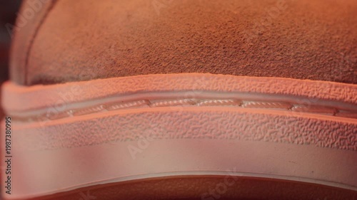 Sneaker sole stitching closeup showing welt and rubber midsole, textured suede upper and seam detail under warm studio light, product inspection angle
