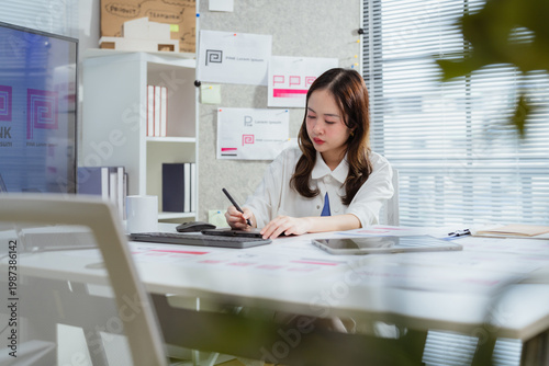 Foto A focused young Asian female entrepreneur using a stylus pen to draw on a digital tablet at her office desk