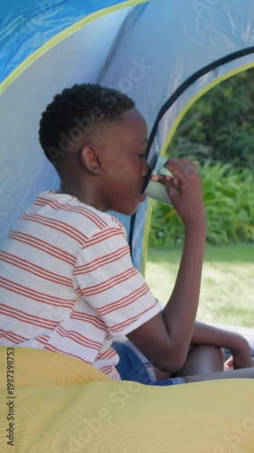 Vertical video: Sipping youth in striped tee raising mug in yard tent, adult hand reaching, bonding