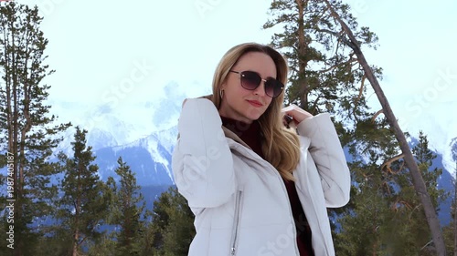 A woman high in the mountains against the backdrop of snow-capped mountains and coniferous trees.