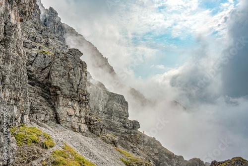 Spectacular Alpine Rock Face of Thaneller Mountain with Hiker in Red, Dramatic Clouds and Blue Sky over the Werner-Riezler-Steig Trail, High Altitude Adventure, Tyrol, Austria, Europe