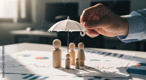 Life insurance concept showing family protection with wooden figures under umbrella on financial documents. Represents coverage, beneficiaries, income security, financial planning