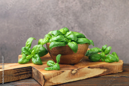 Fresh basil leaves and bowl on wooden table against grey textured background, closeup