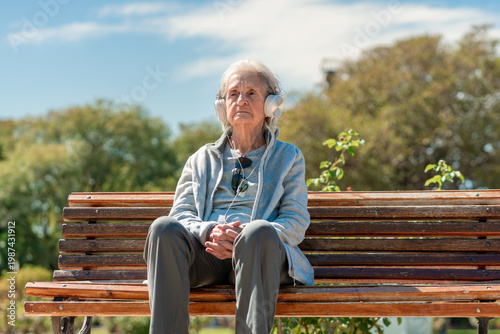 Elderly woman with headphones enjoying music while sitting on a park bench