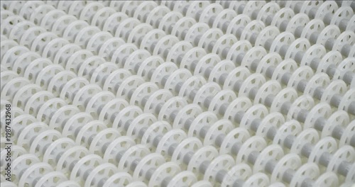 An industrial conveyor is in operation, white plastic rollers are rotating. Static handheld shot of production, sorting, or transportation line, real time speed, artificial lighting.