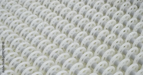 An industrial conveyor is in operation, white plastic rollers are rotating. Static handheld shot of production, sorting, or transportation line, real time speed, artificial lighting.