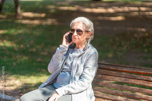Tableau sur toile An 85 year old grandmother talks on her phone while sitting on a park bench with