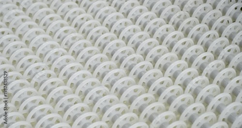 An industrial conveyor is in operation, white plastic rollers are rotating. Static handheld shot of production, sorting, or transportation line, real time speed, artificial lighting.