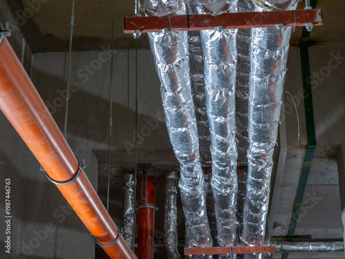 Industrial pipeline system with thermal insulation and drainage pipes on ceiling.  The image shows several air ventilation ducts or water pipes wrapped in shiny silver thermal insulation foil