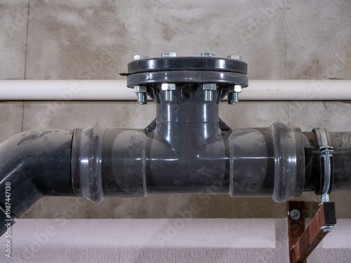 Industrial plastic pipe flange connection with bolts in building utility system. A close-up shot of a grey PVC or HDPE industrial pipe fitting with a flanged T-junction