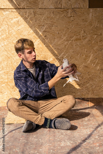 A young man sits cross-legged on the floor, holding a white pigeon in his hands